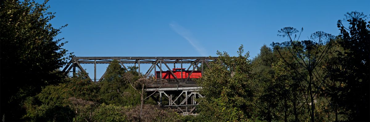 Dieses Panorama, bei dem gerade ein roter Zug über eine Eisenbahnbrücke fährt besteht aus 6 hochkant aufgenommenen Fotos.